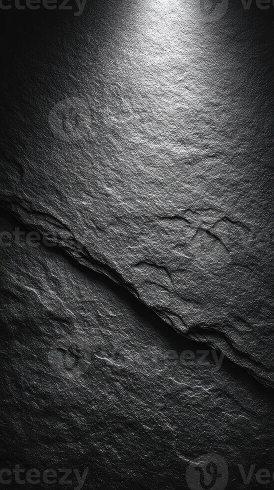 Textured dark stone surface illuminated by soft light highlighting its natural pattern photo