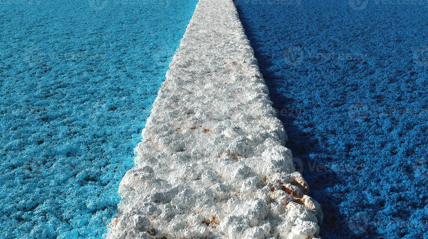 Coastal view of a striking blue waterway with a rocky pathway extending through vibrant turquoise waters at mid-day photo