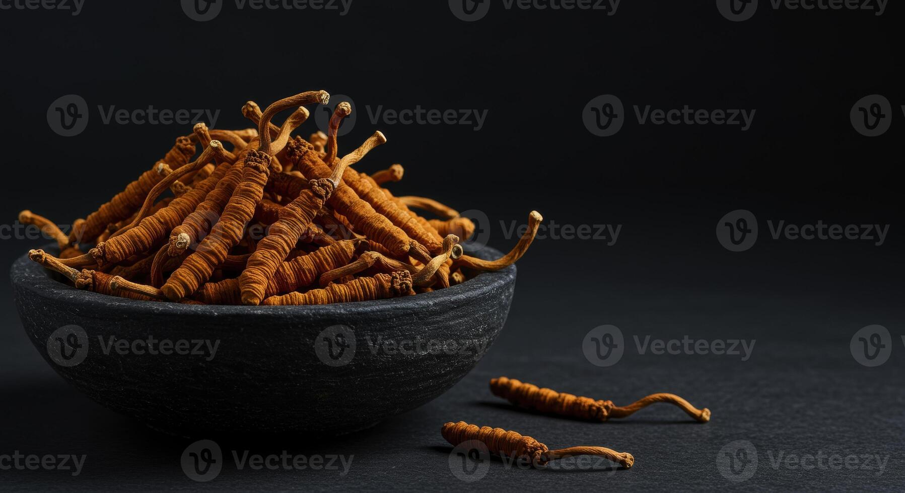 Dried Cordyceps Sinensis Mushrooms in a Dark Stone Bowl with Pieces on Black Surface photo