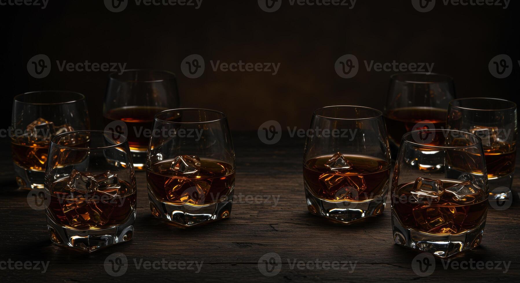 Multiple glasses of amber spirit with ice on a dark wooden table photo