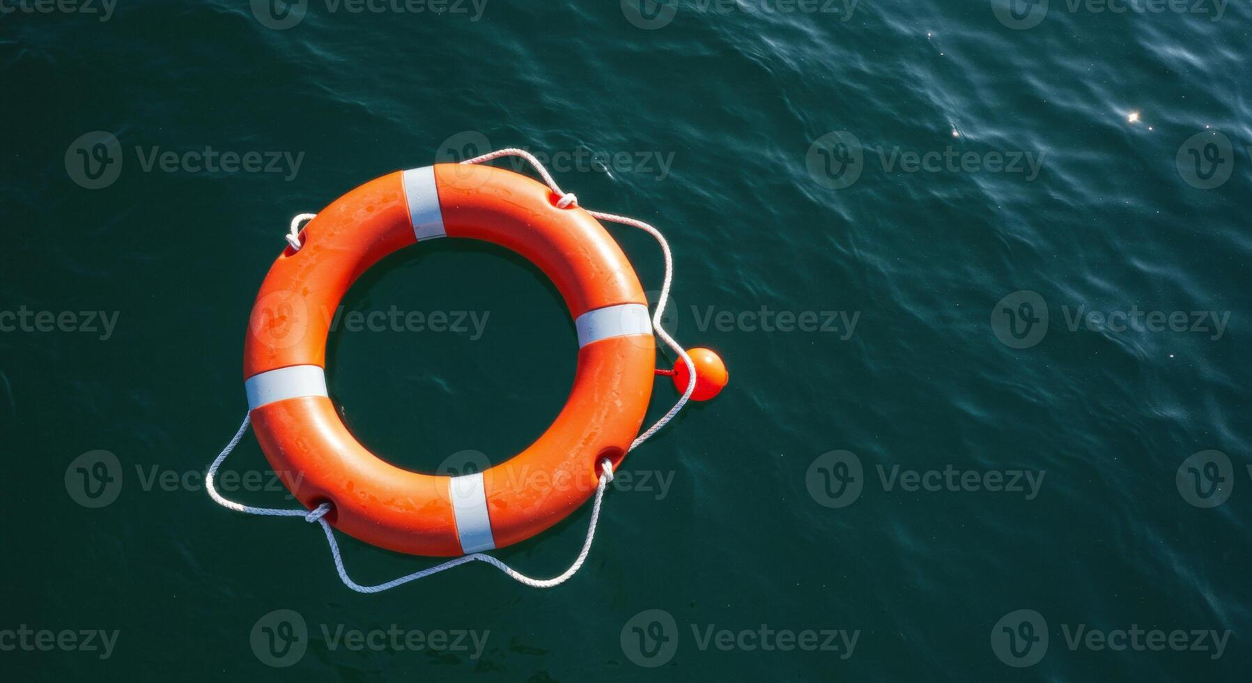 Bright orange lifebuoy with white stripes floating on calm dark water photo