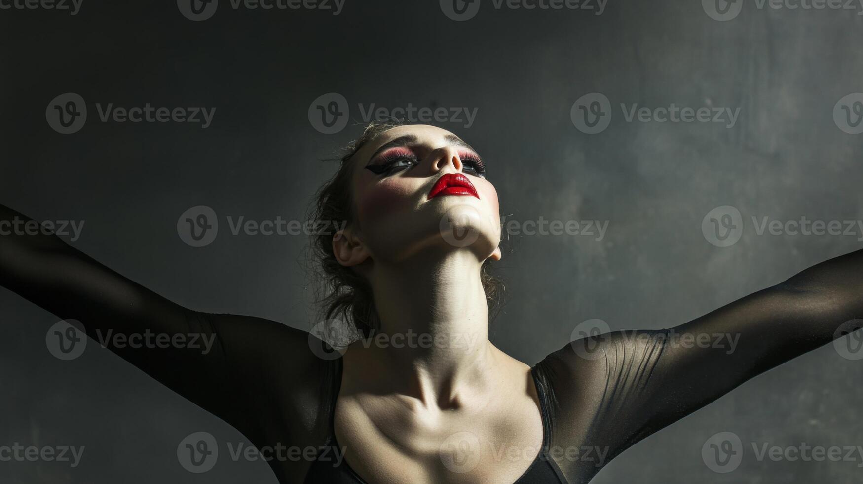 Woman with dramatic makeup and a black outfit posing against a gray background photo