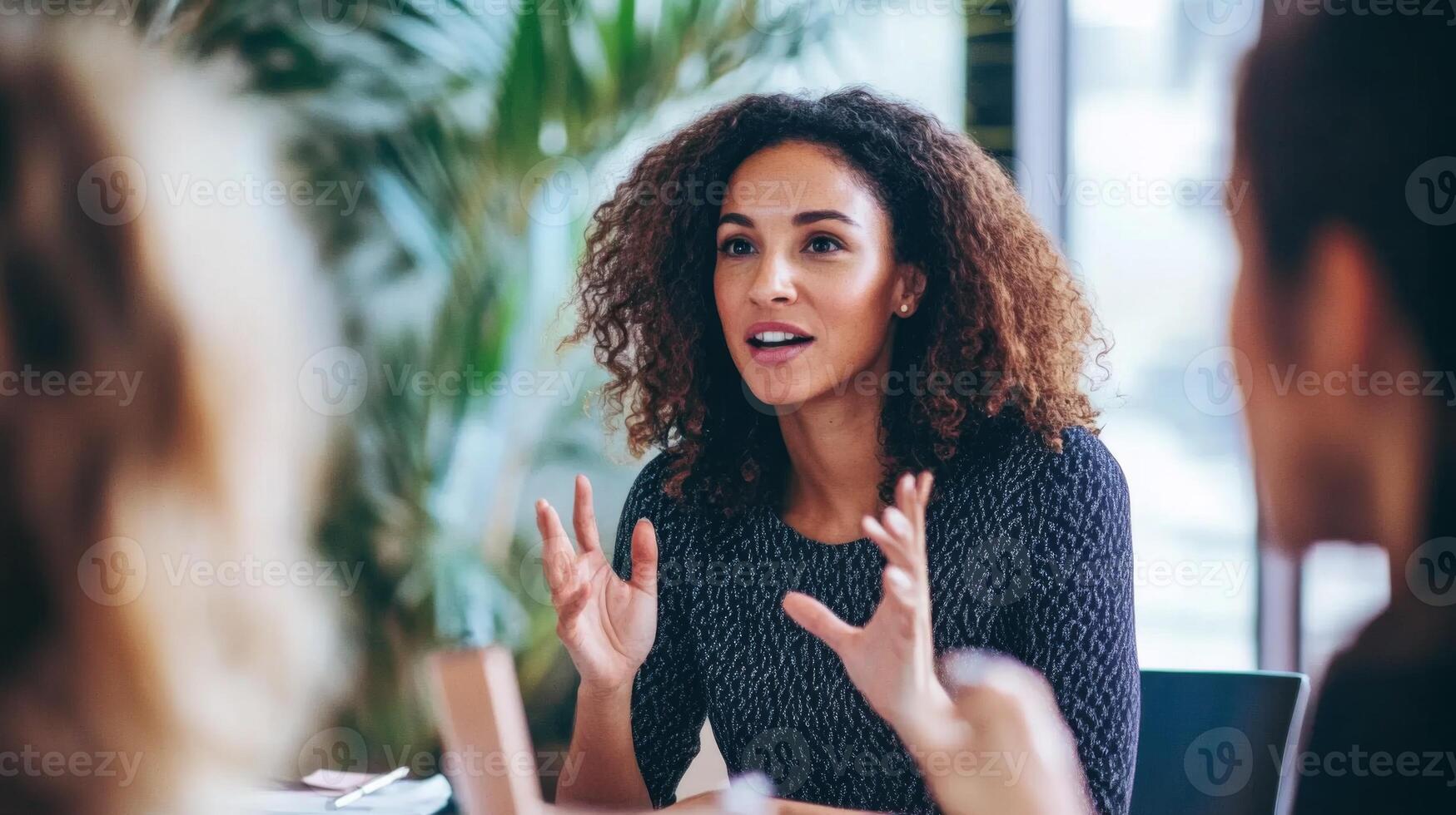 Woman with curly hair gesturing while speaking to a group photo