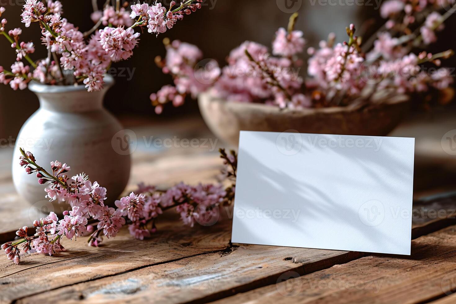 A blank card is sitting on a table with a vase of pink flowers photo