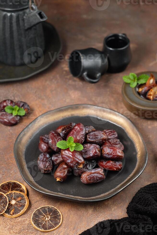 Kurma, or dates, are sweet fruits from the date palm tree, commonly enjoyed fresh or dried - photographed on a black plate decorated with fresh mint leaves, against a wooden plank background photo
