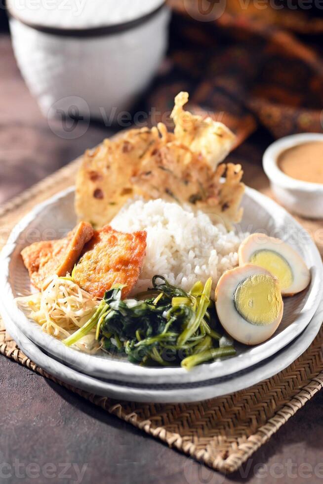 Nasi Pecel is traditional Javanese rice dish of steamed rice with vegetables salad, peanut dressing, tempeh, bean curd and peanut crackers known as peyek photo