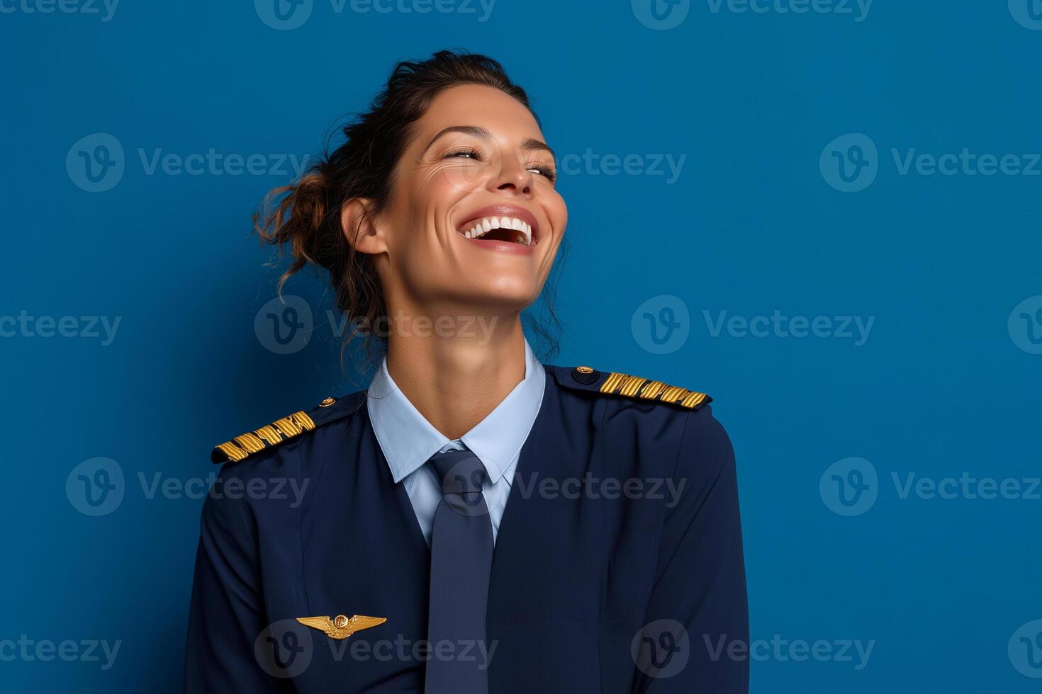 Joyful female pilot smiling in crisp uniform against a solid cobalt blue background photo