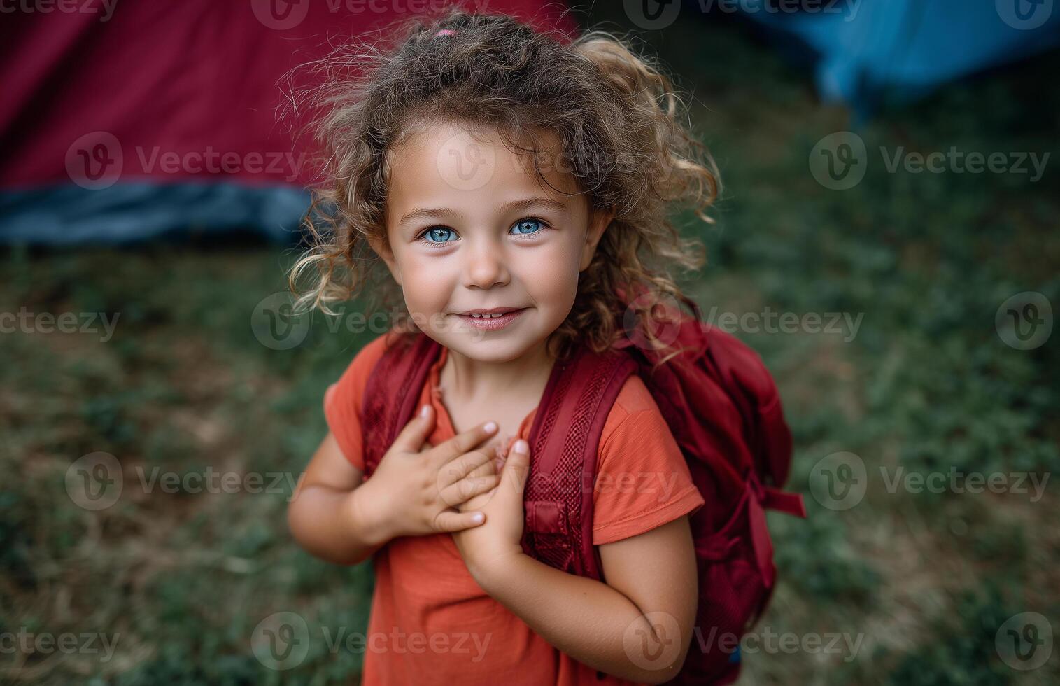 Smiling little girl at outdoor campsite with backpack in front of colorful tents photo