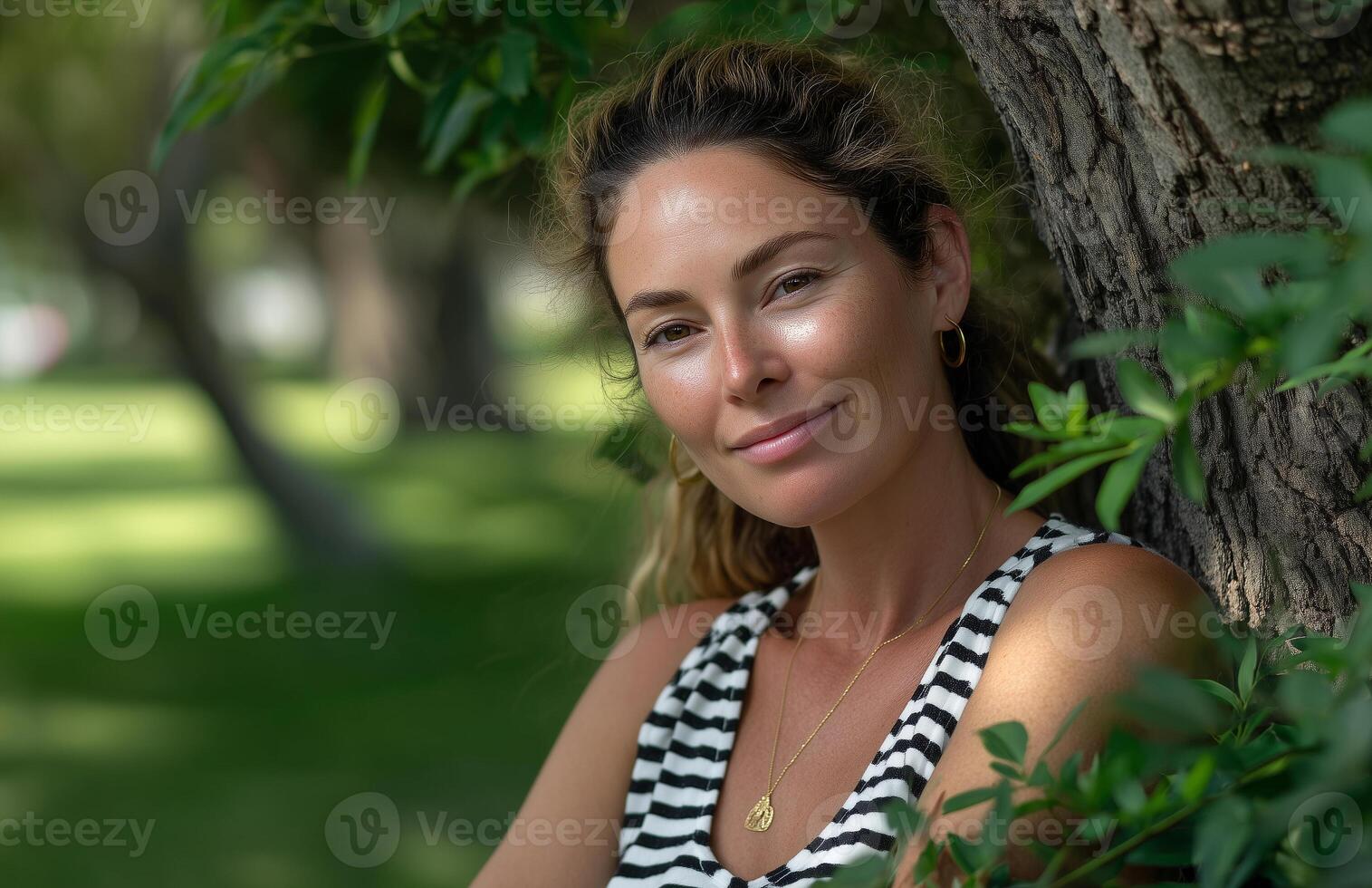 Woman enjoys warm summer day leaning against oak tree in striped tank top amidst green foliage photo