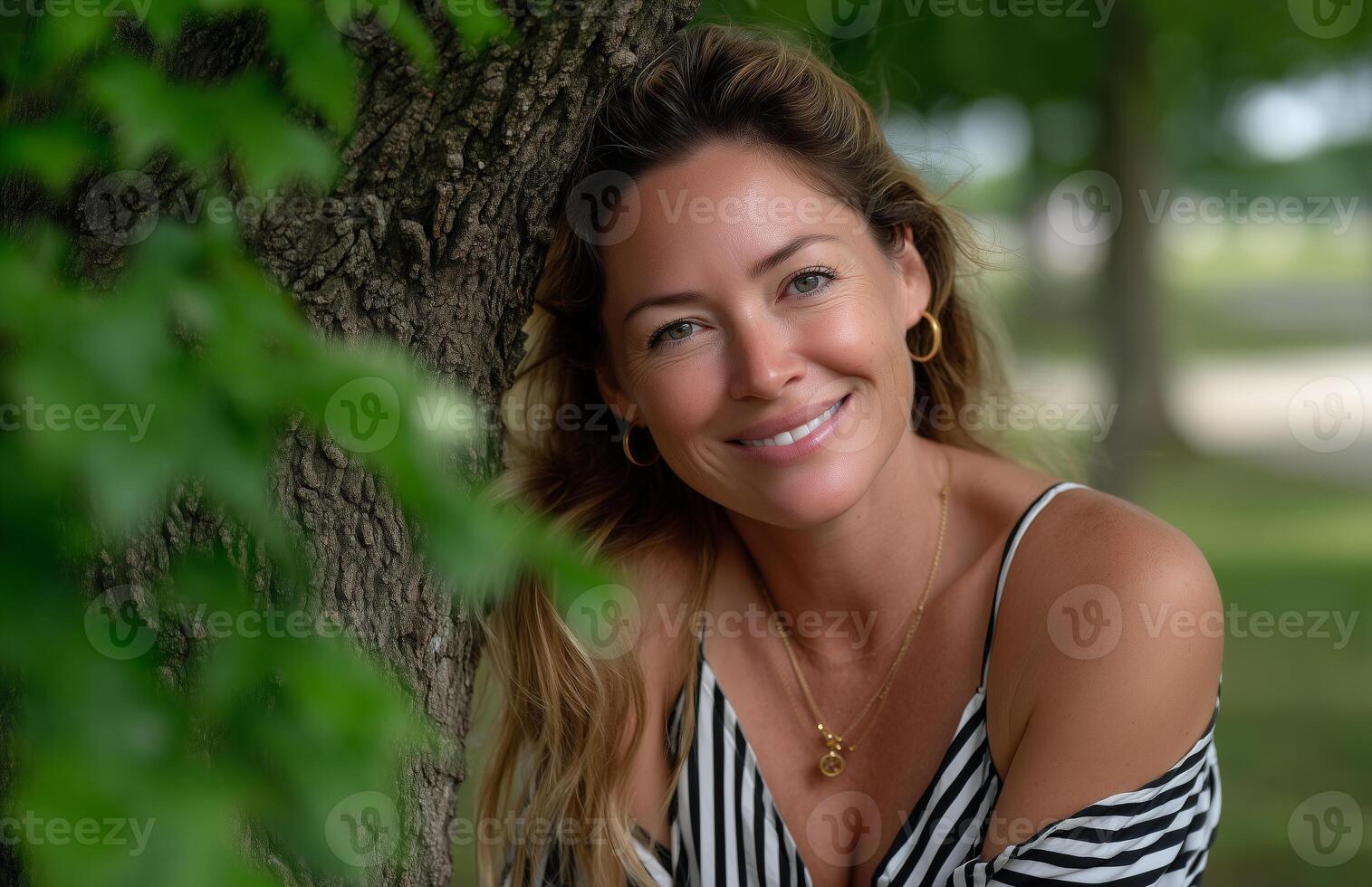 Woman enjoys a summer day in black and white striped tank top leaning against oak tree photo