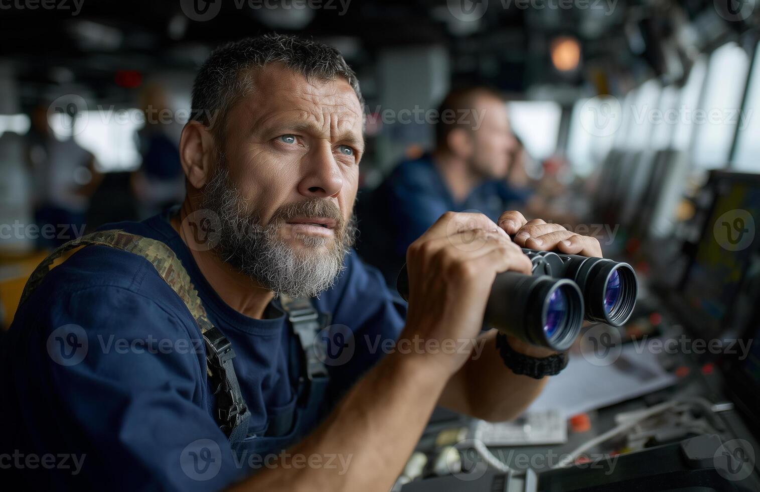 Male captain in blue overalls uses binoculars on ship bridge with advanced navigation equipment photo