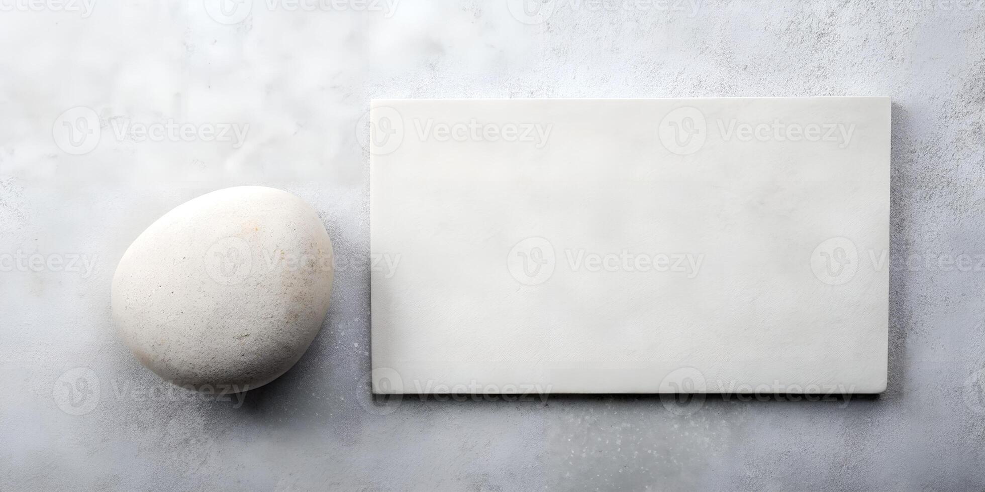 Minimalist Composition of a Smooth Pebble Next to a Blank White Rectangle on a Textured Gray Surface for Creative Design Use photo