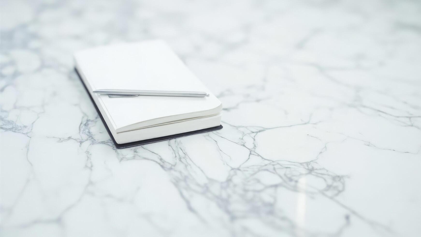 Minimalist composition featuring a blank white notebook and pen resting on a marble surface photo