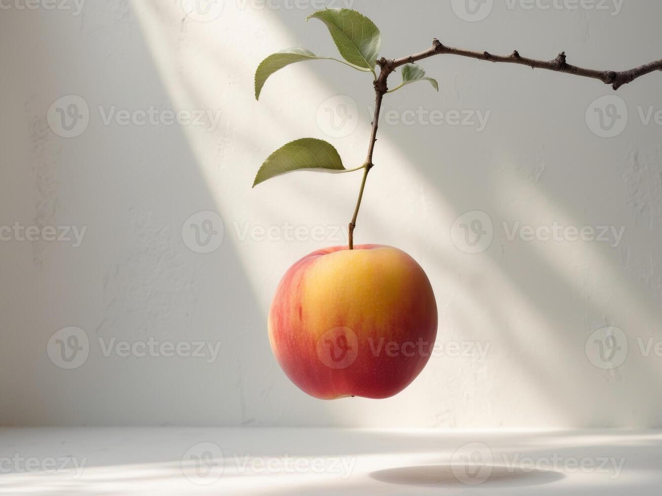 An apple hanging from a branch on a white table photo