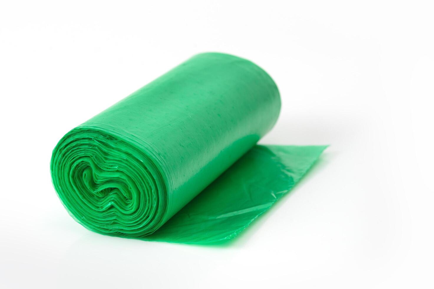 Green plastic garbage bag roll unrolled on white background, household waste bag for cleaning or trash disposal. photo