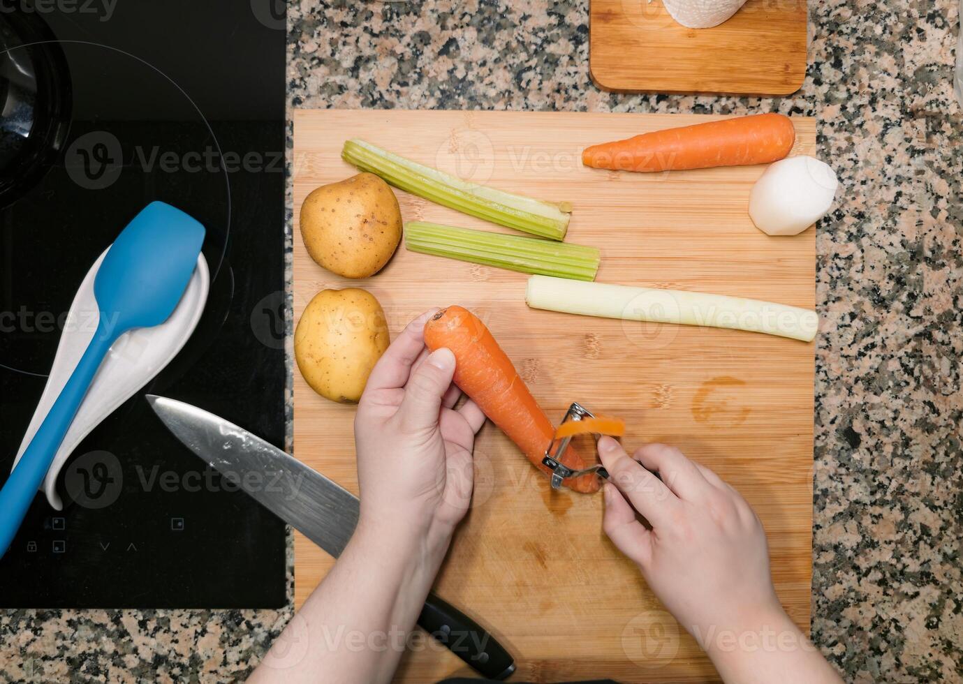 Chefs hand peeling a carrot against wood cutting board at home kitchen. photo