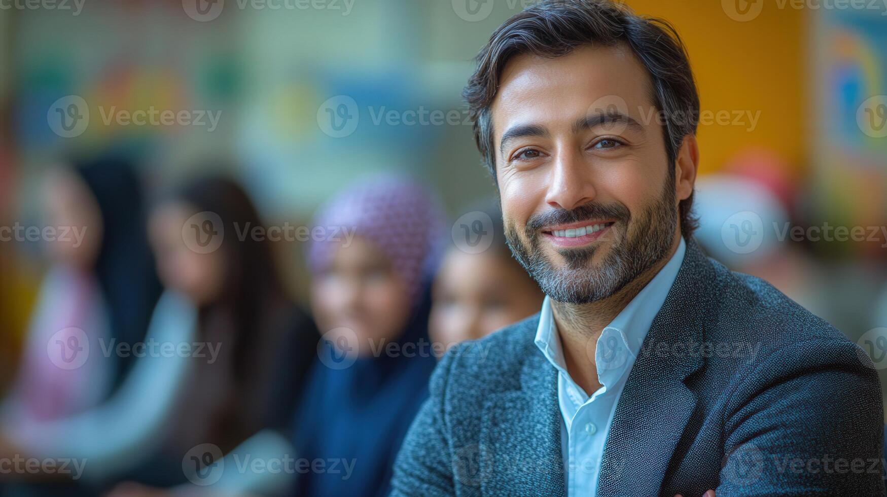 A confident teacher smiles broadly with his students blurred in the background of the classroom. photo