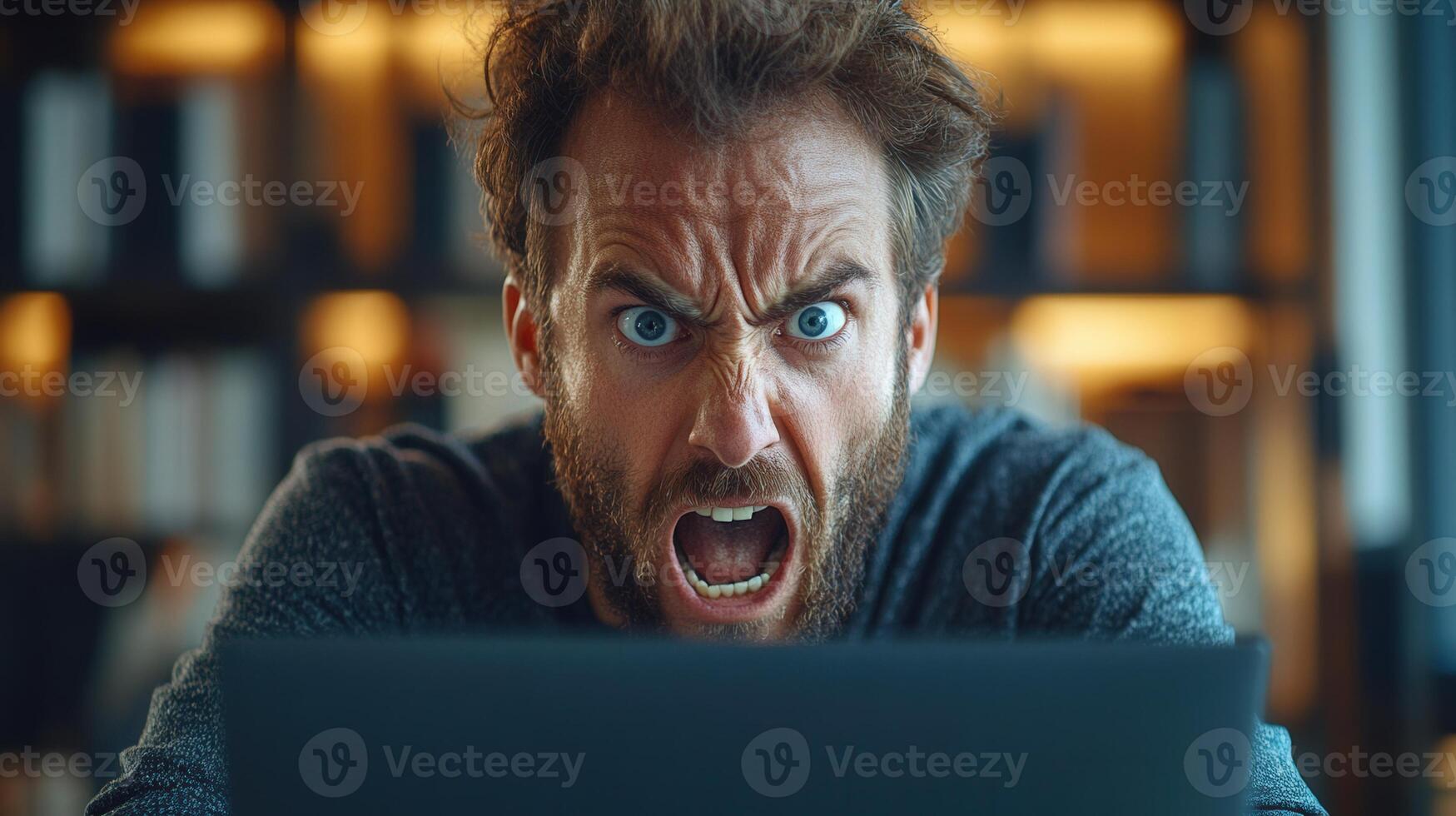 An angry man yells in frustration at his computer, showing intense emotions. photo