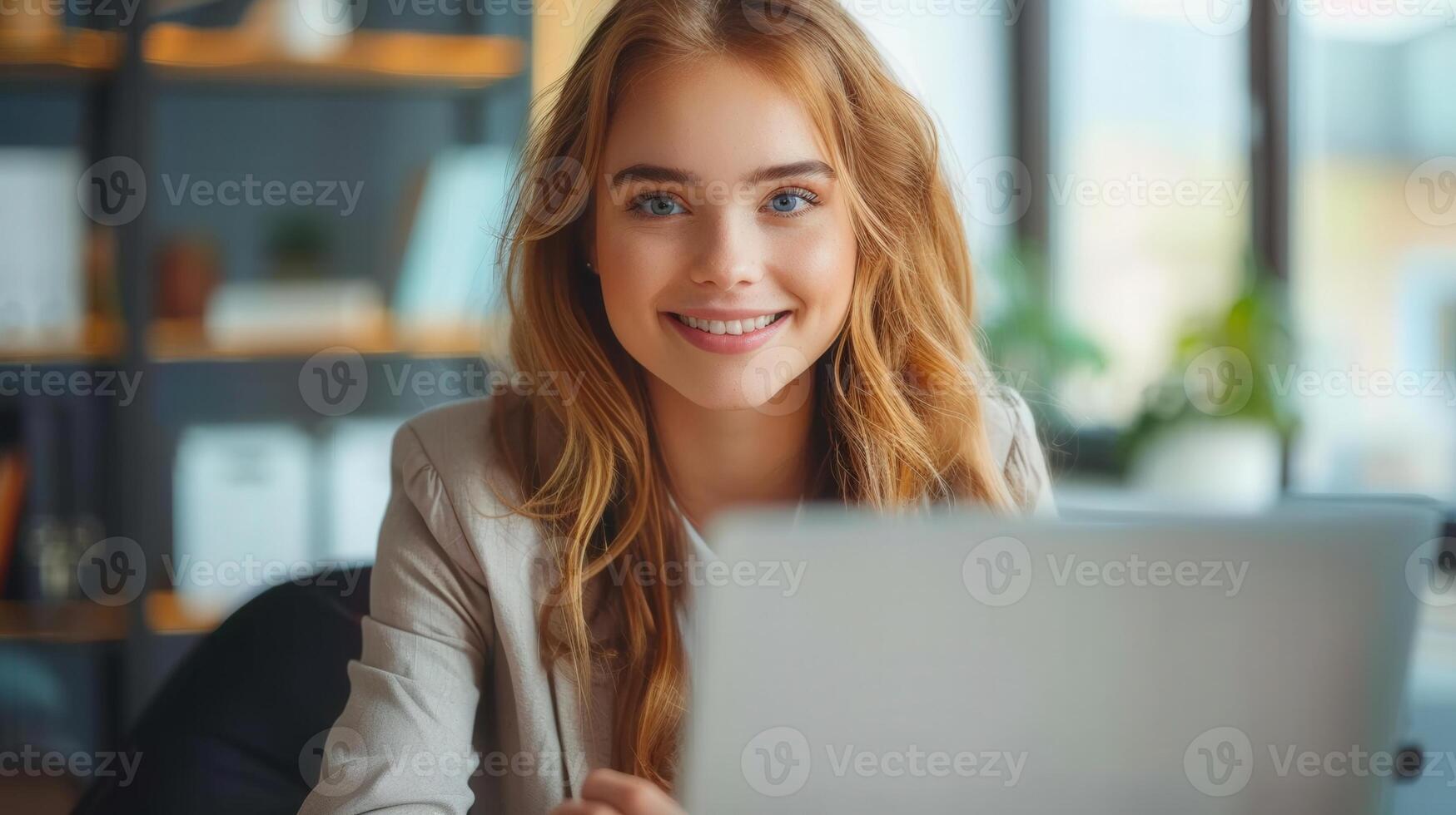 Smiling young woman looks towards the camera while sitting at a computer in the office. photo