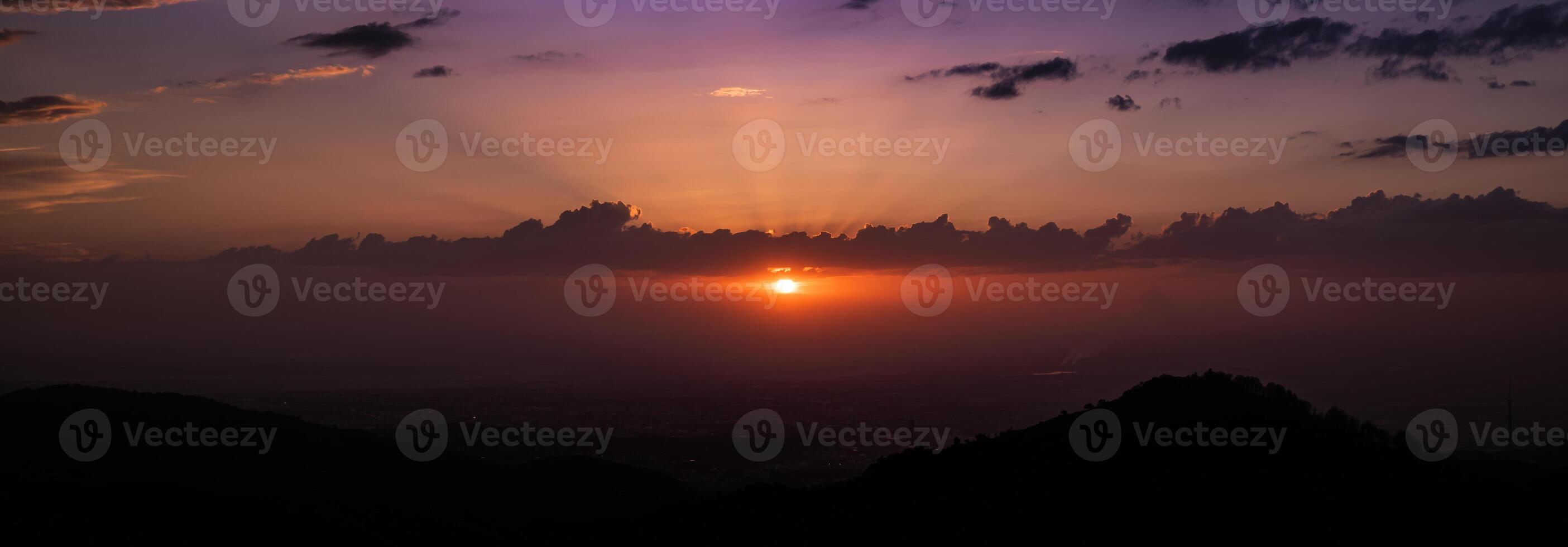 Dramatic sunset over mountain silhouette with vibrant purple and orange sky, panoramic twilight landscape photo