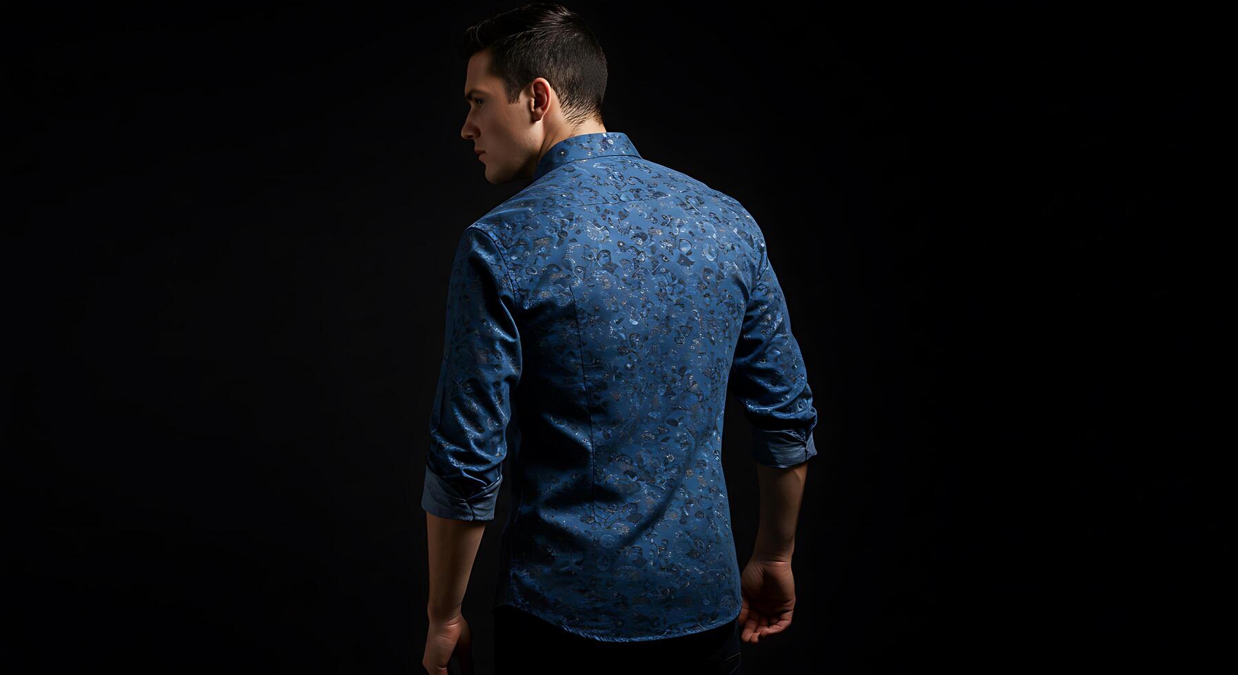 A man in a blue shirt standing against a black background photo