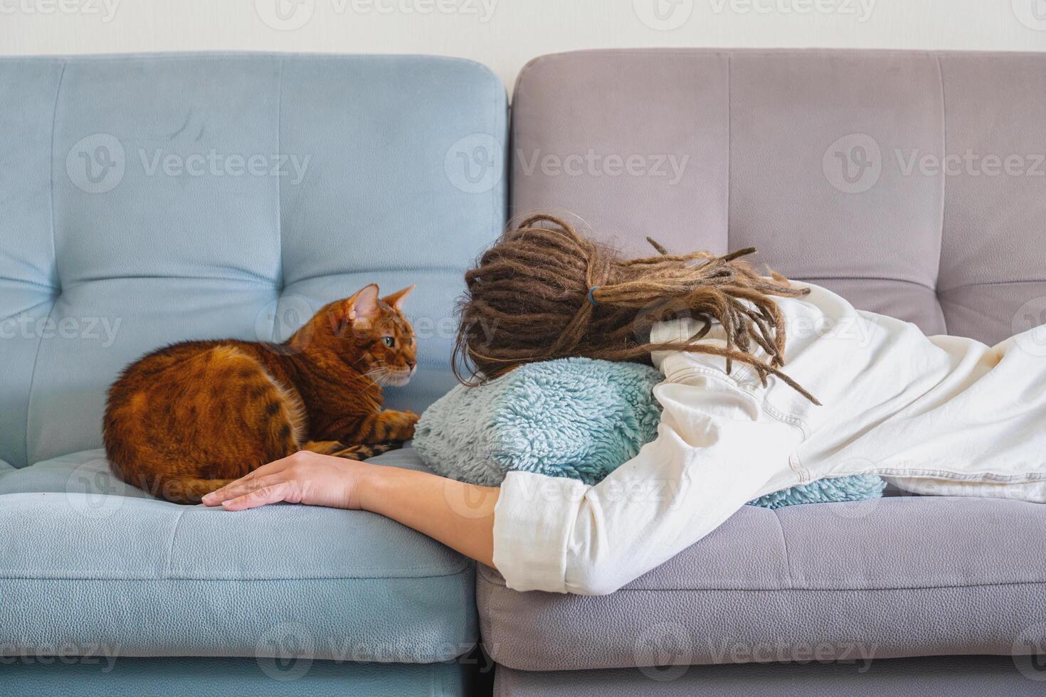 Woman with Dreadlocks Sleeping on Sofa with Cat Relaxing Next to Her. photo