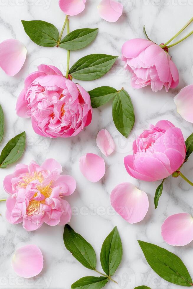 Pink peonies with lush green leaves and scattered petals are artistically arranged on a marble surface, creating a vibrant and elegant floral composition for decoration or design photo
