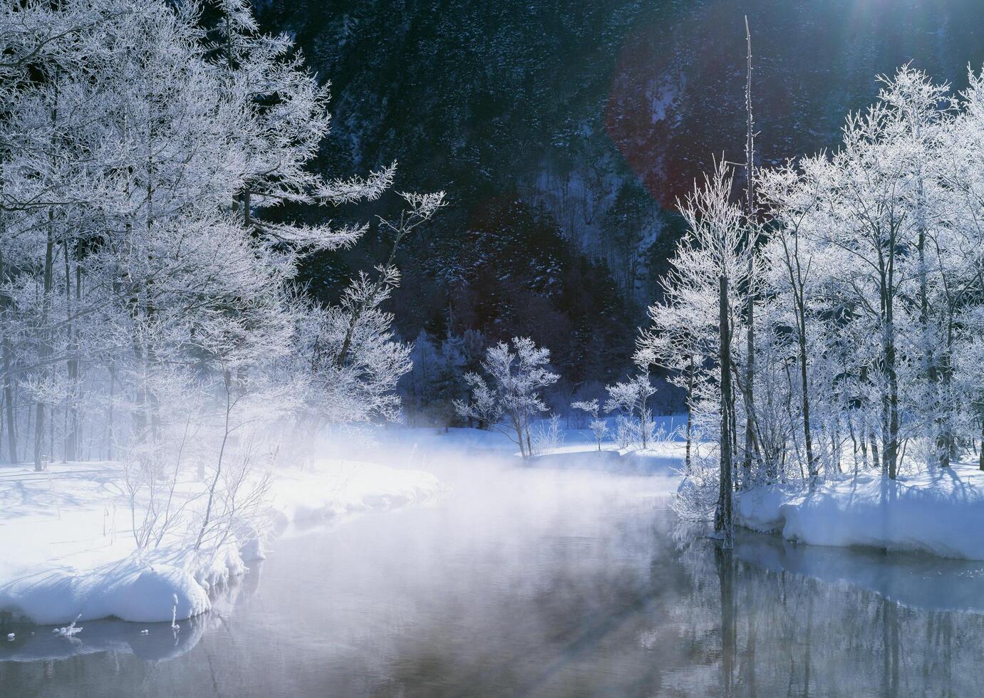 a river in the snow with trees and sun shining photo