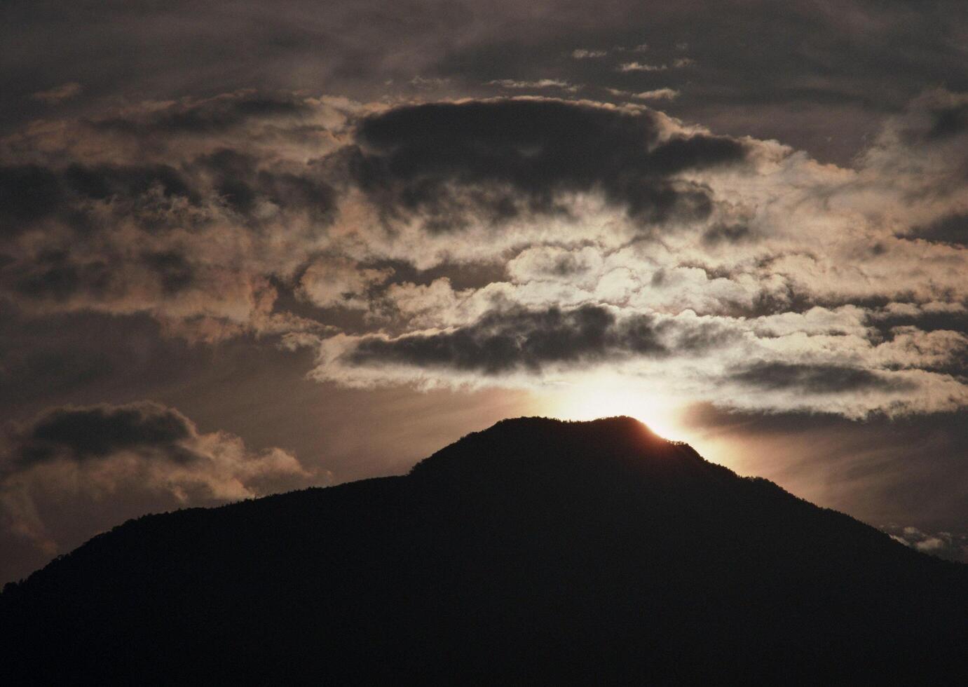 the sun is setting behind a mountain with clouds photo