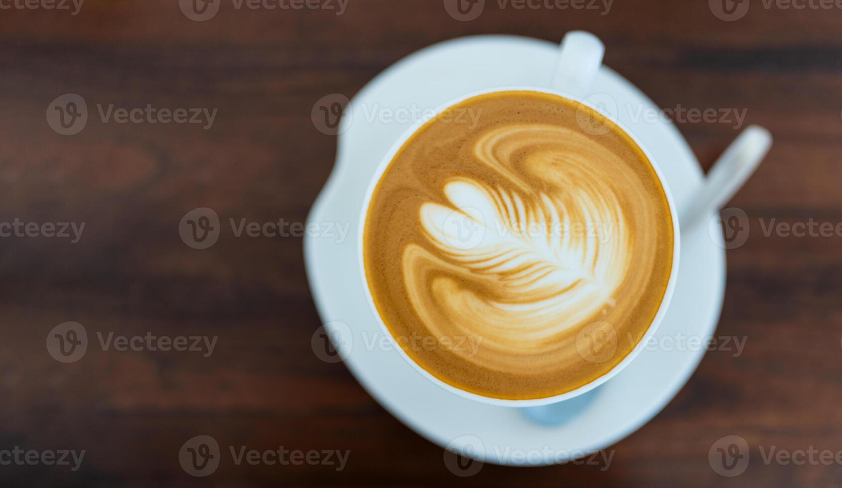 Steaming cup of latte with latte art on a wooden table in a cozy cafe setting. photo