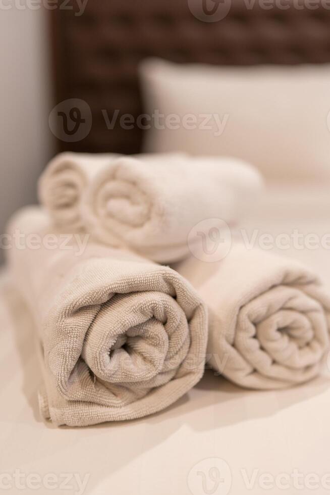 Clean folded rolled white towels prepared on the bed in hotel room photo