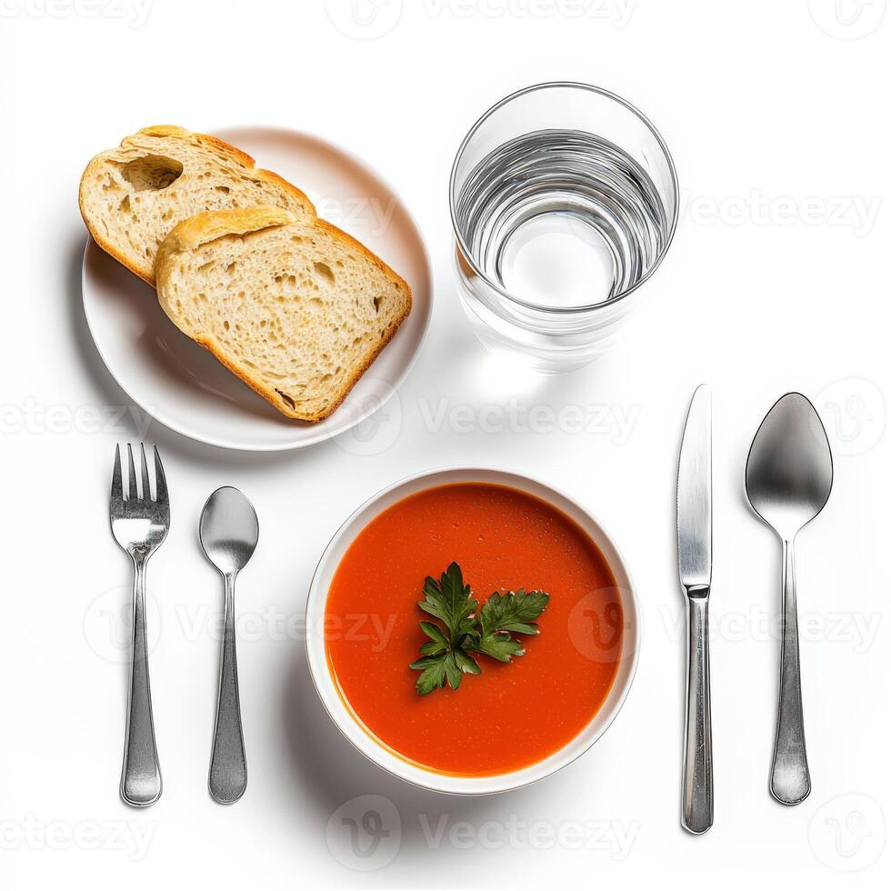 A bowl of tomato soup, bread and silverware on a white table photo