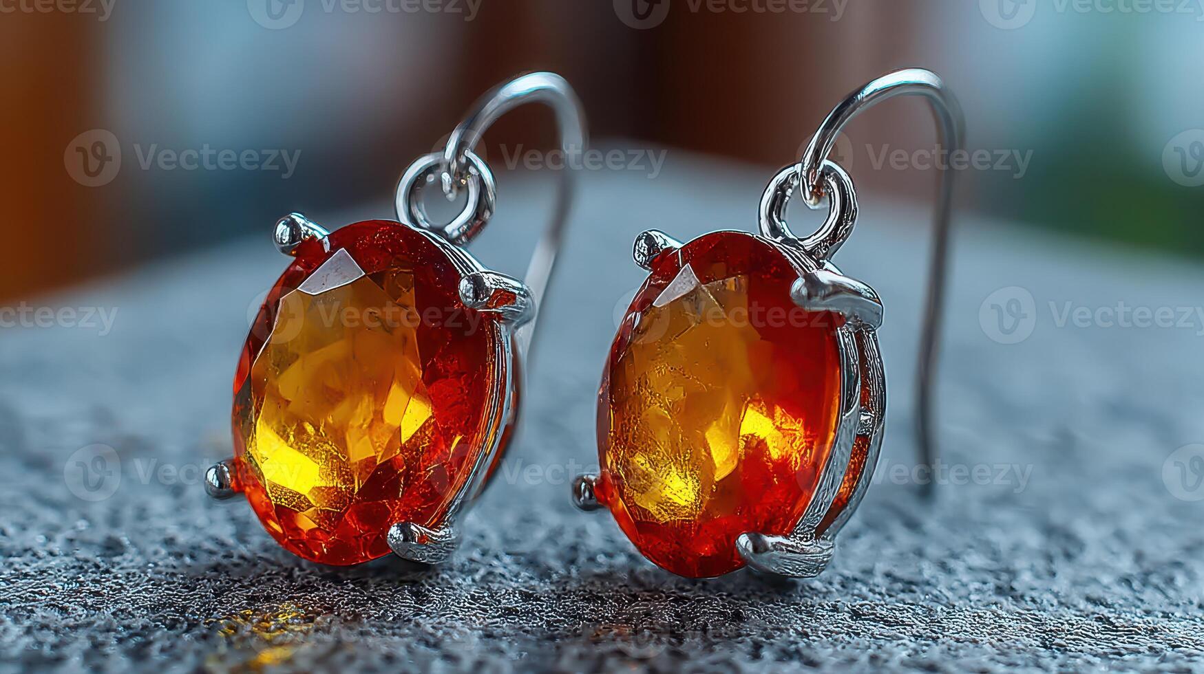 Sparkling red and orange gemstone earrings displayed on a textured surface with a blurred background photo