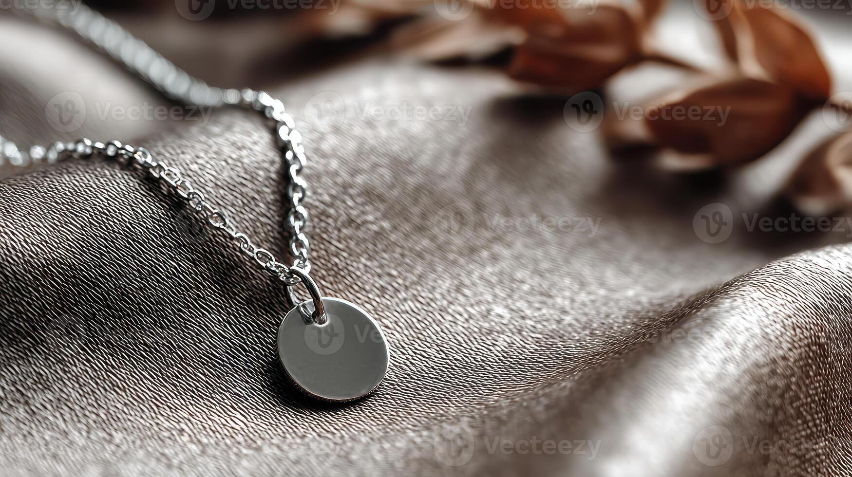 Silver pendant necklace resting on soft satin fabric with dried flowers in background during warm sunlight photo