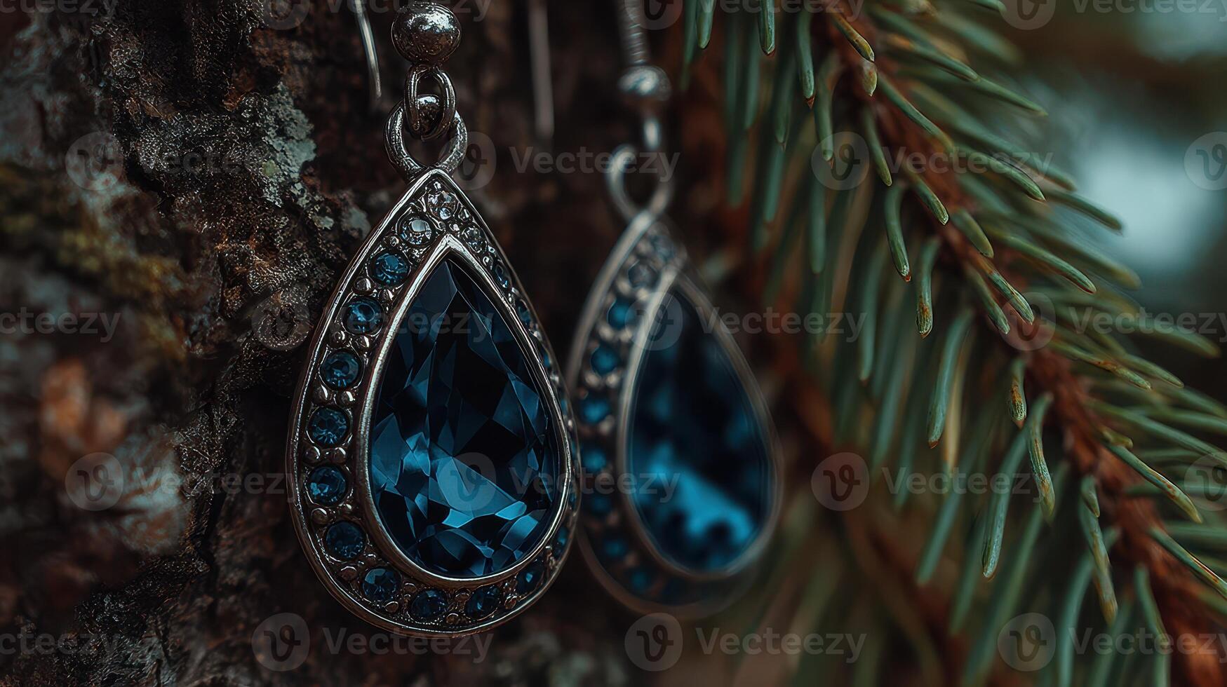 Elegant blue teardrop earrings hanging from a pine tree branch in a serene outdoor setting photo