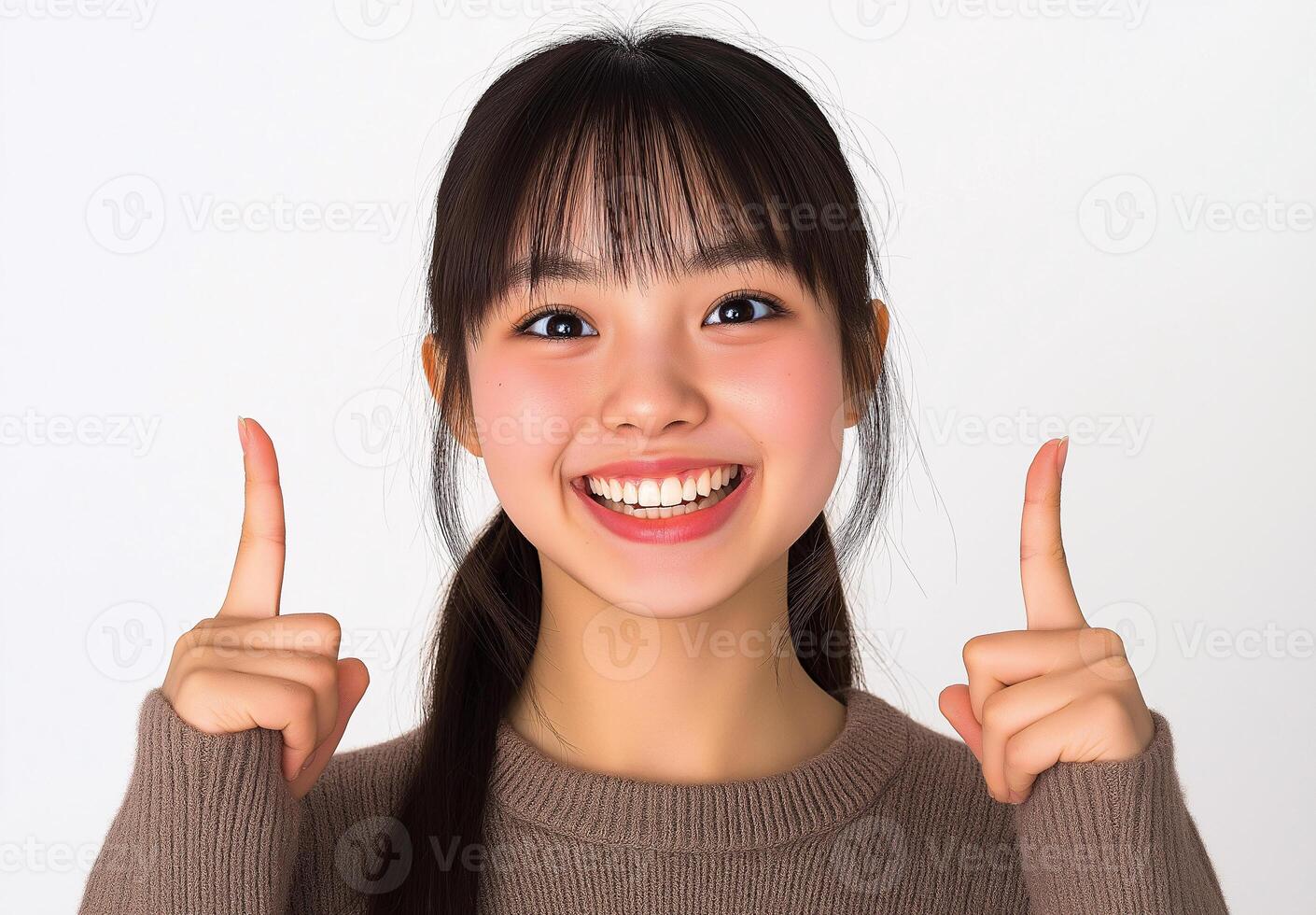A joyful young girl in a cozy sweater pointing upward with a beaming smile against a bright, neutral background photo