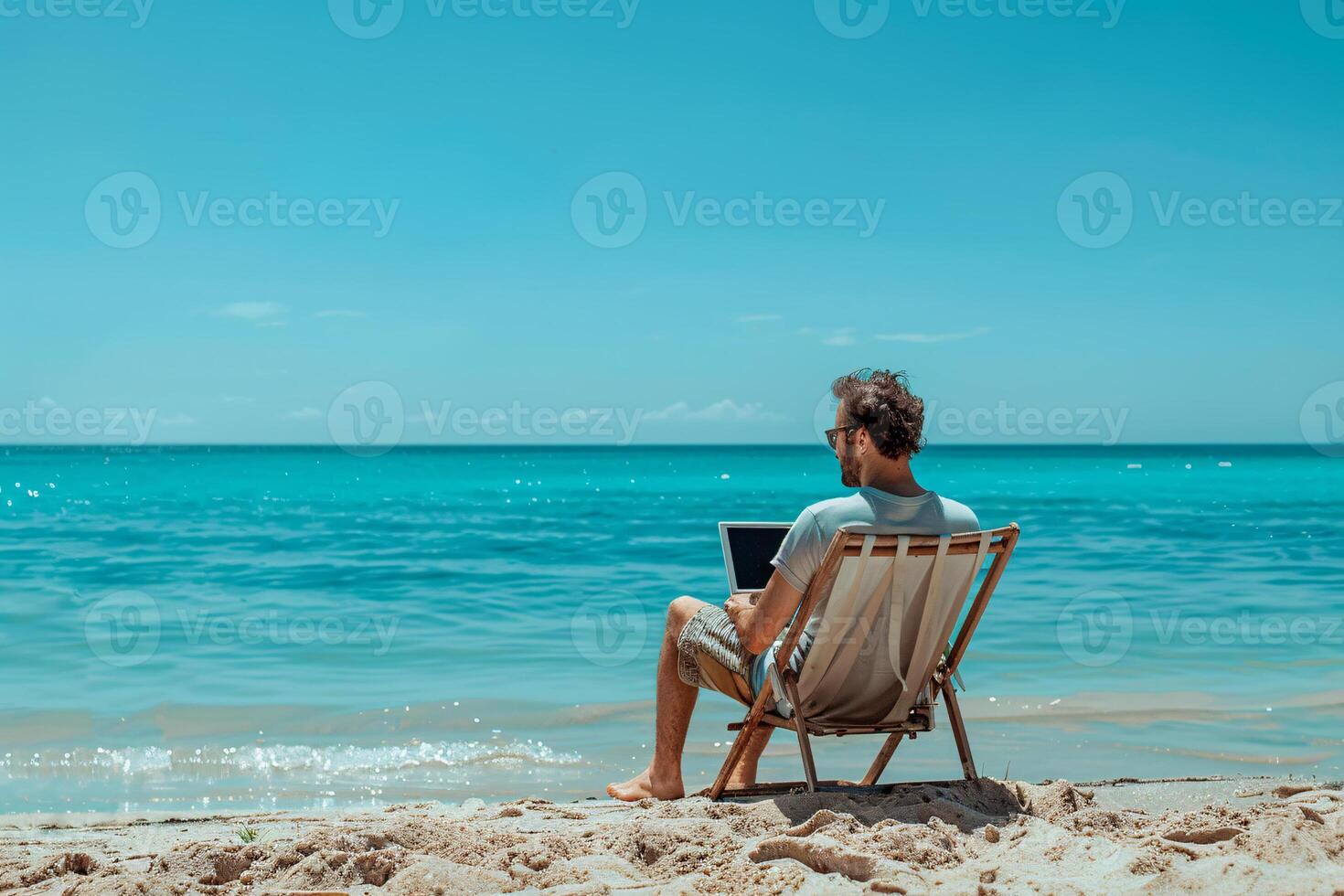 A man is sitting on a beach chair with a laptop in front of him photo