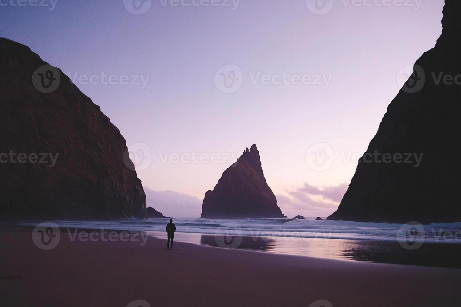 A person standing on the beach near a large rock photo