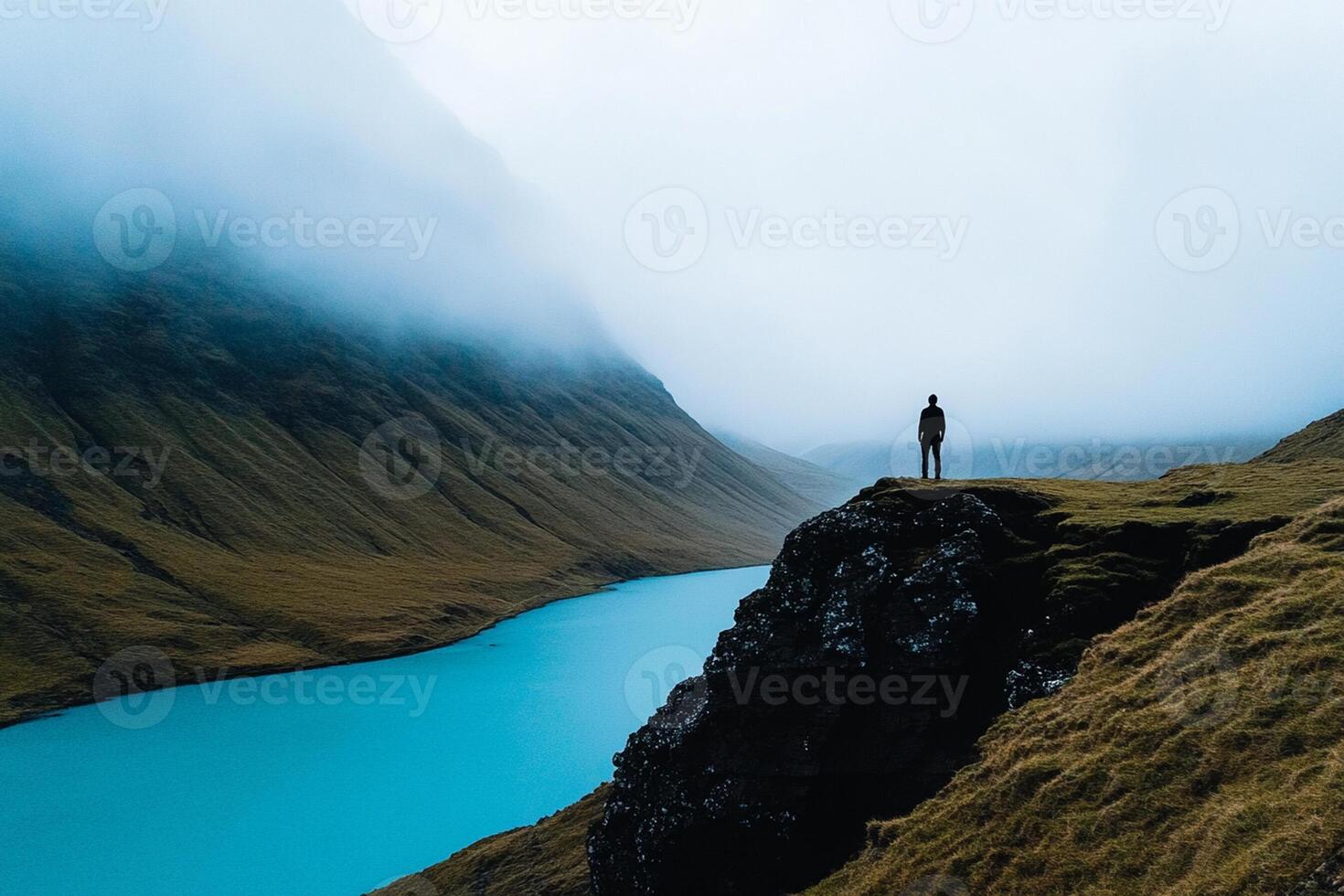 A person standing on a cliff overlooking a lake photo