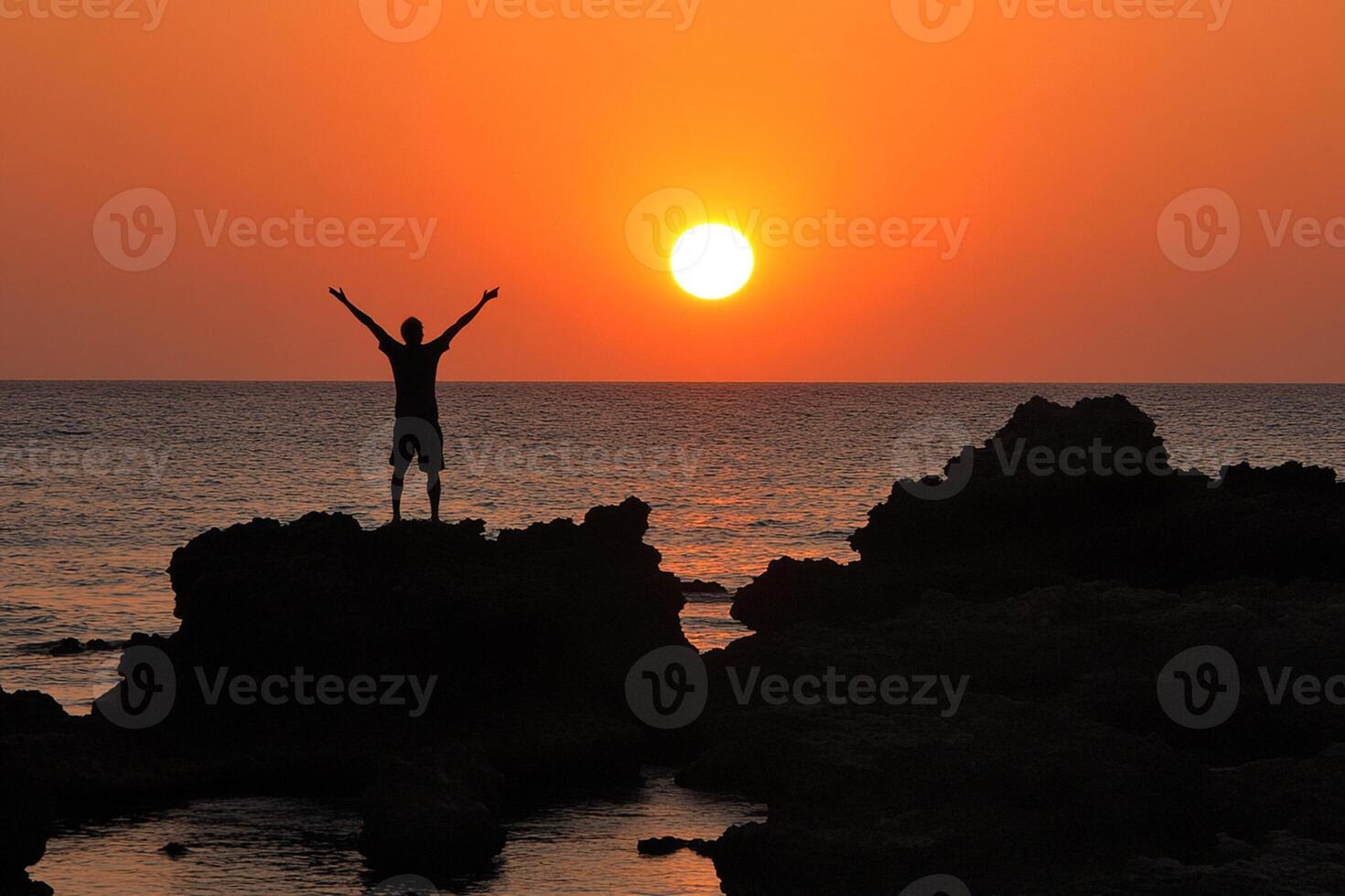 A person standing on a rock at sunset photo