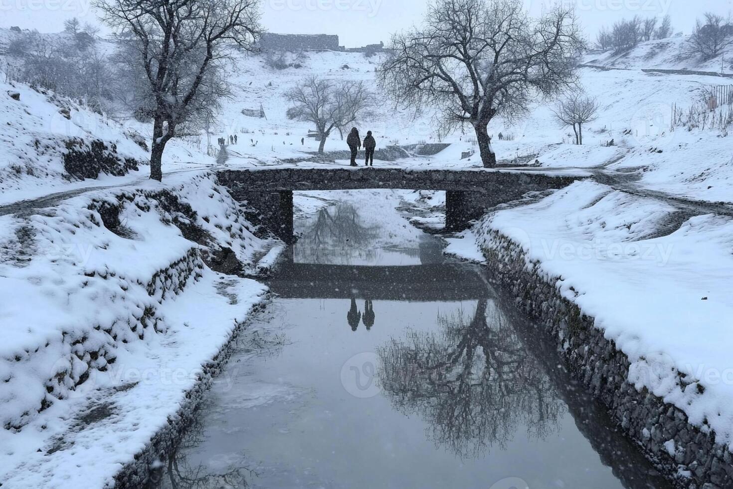 Two people walk across a bridge over a small stream photo