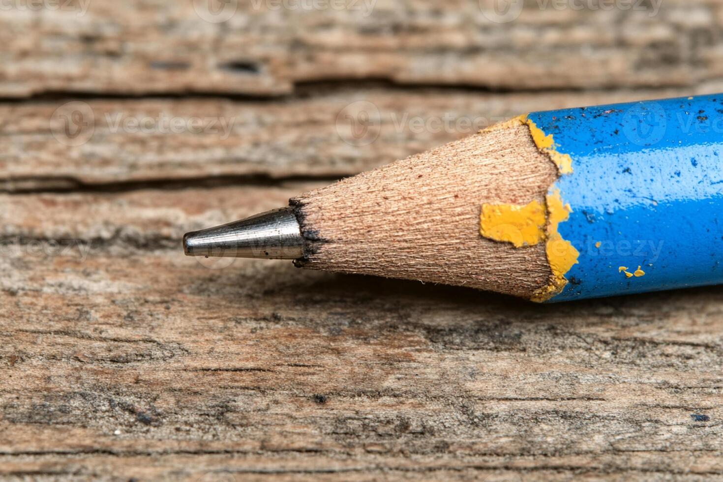 A blue pencil with a yellow tip sitting on a wooden surface photo