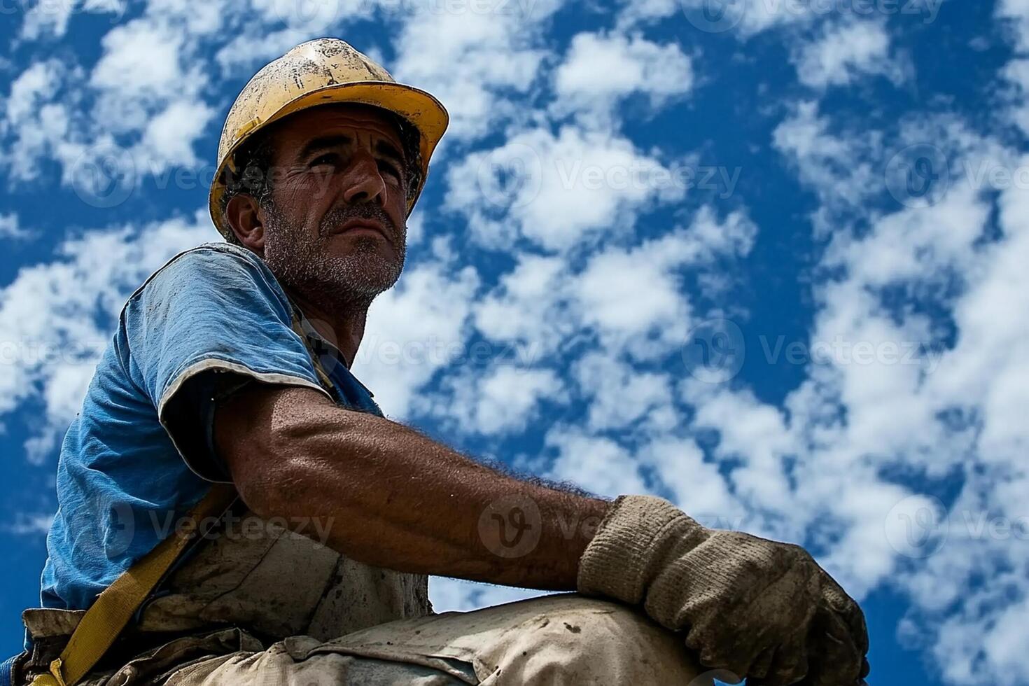 A man in a hard hat and safety glasses sits on a ladder photo
