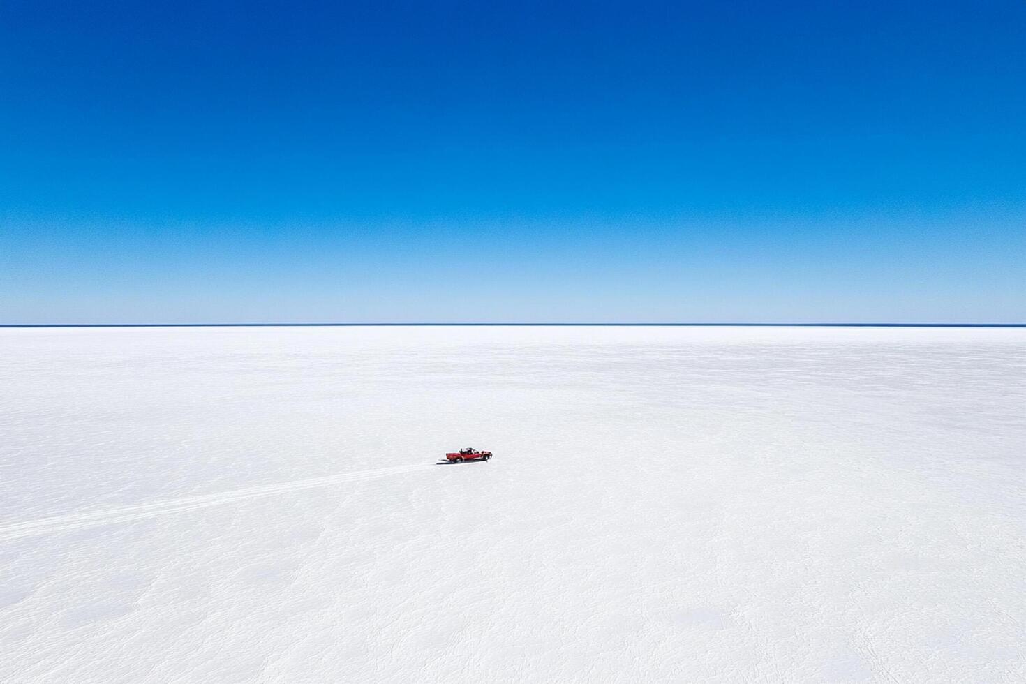 A red car is driving across a large white field photo