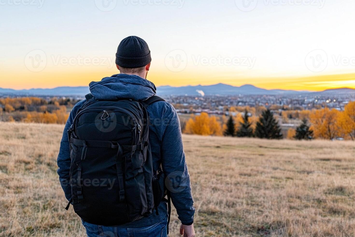 A man with a backpack standing in a field looking at the sunset photo