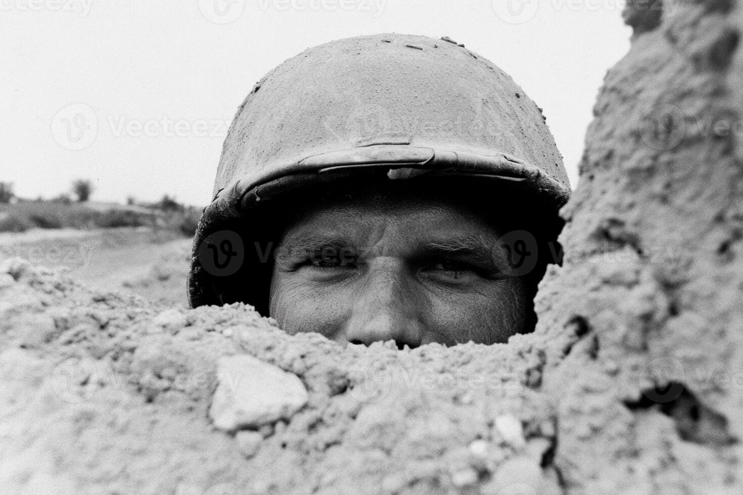A man in a helmet peeking out from a hole in the sand photo