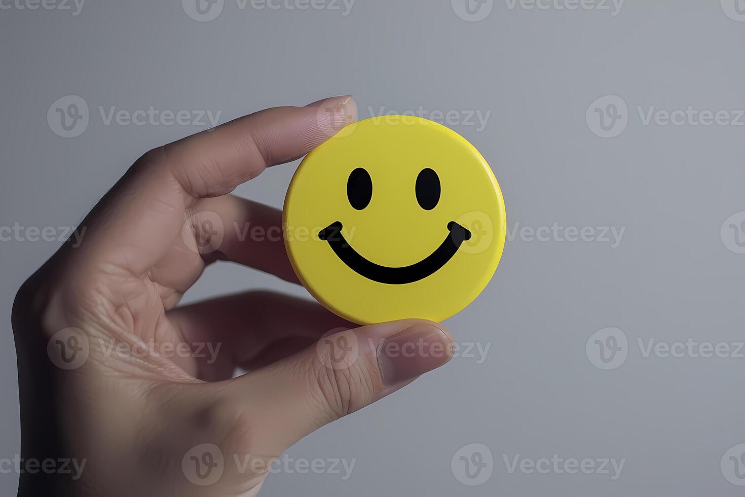 Hand holding yellow round button with smiley face, expressing happiness and positivity photo