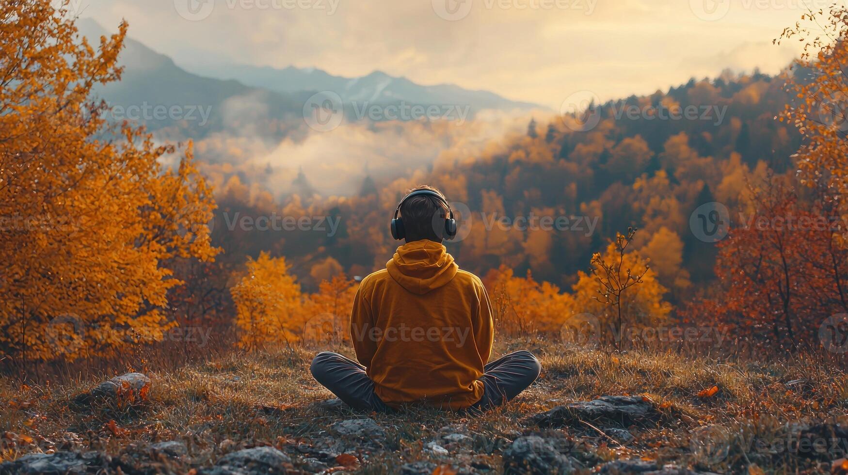 A person sitting in the middle of a field with autumn trees in the background photo