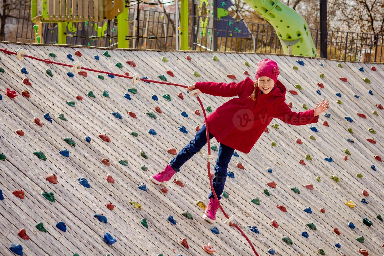 Happy child climbing on artificial rock wall using rope on playground photo