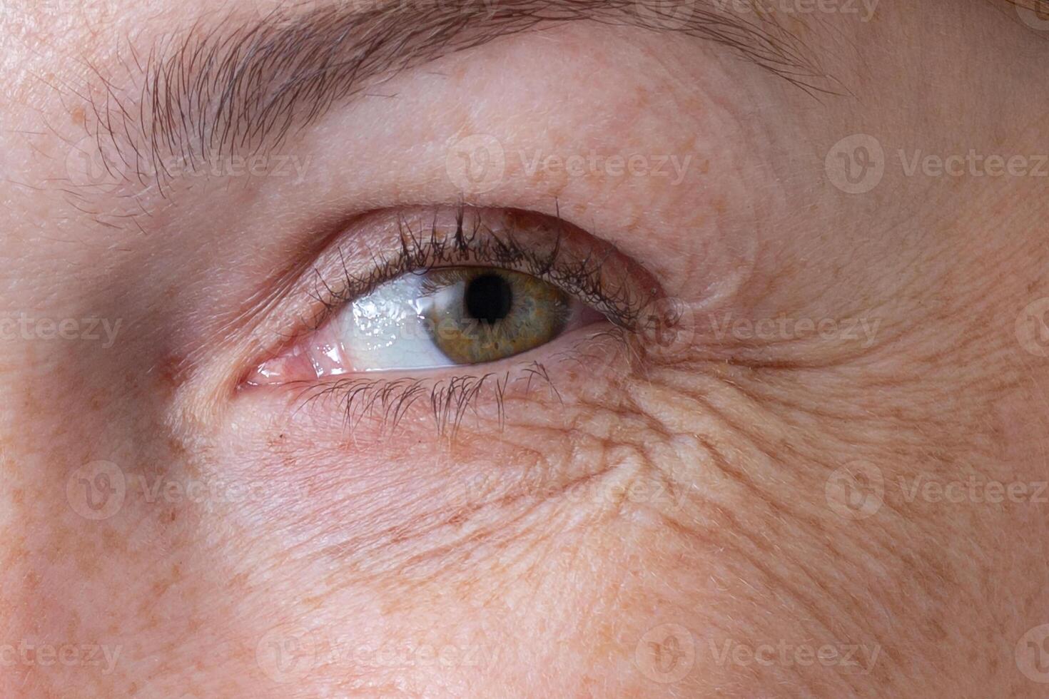Cropped eye with wrinkles of middle aged caucasian woman smiling and looking at camera showing crow's feet photo